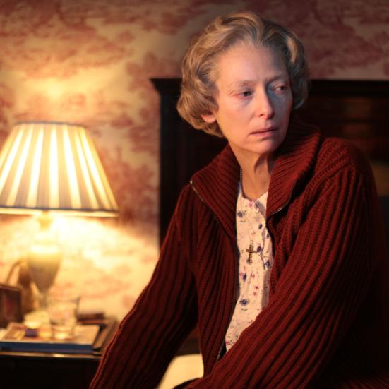 Stillbillede af Tilda Swinton fra filmen, siddende på sengekant i dæmpet belysning
