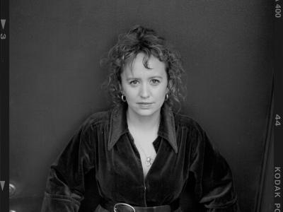 Sort-hvidt portræt af forfatteren Olga Ravn i mørk kjole med bælte, stående foran en mørk baggrund.